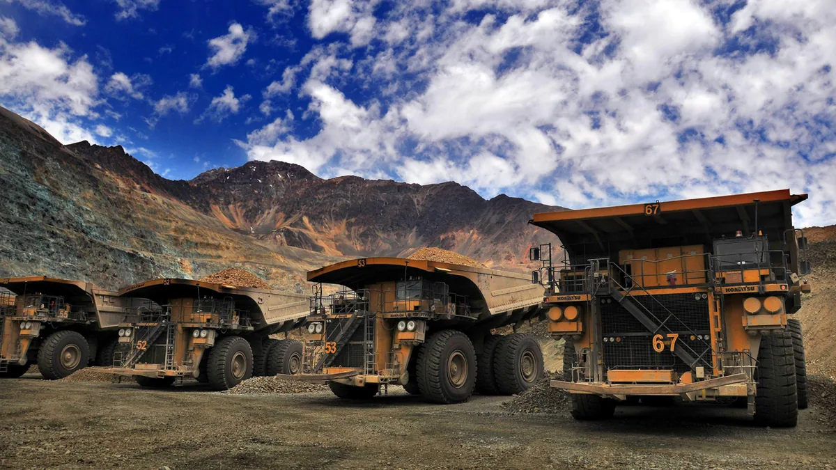 Mining haul trucks lined up under mountains